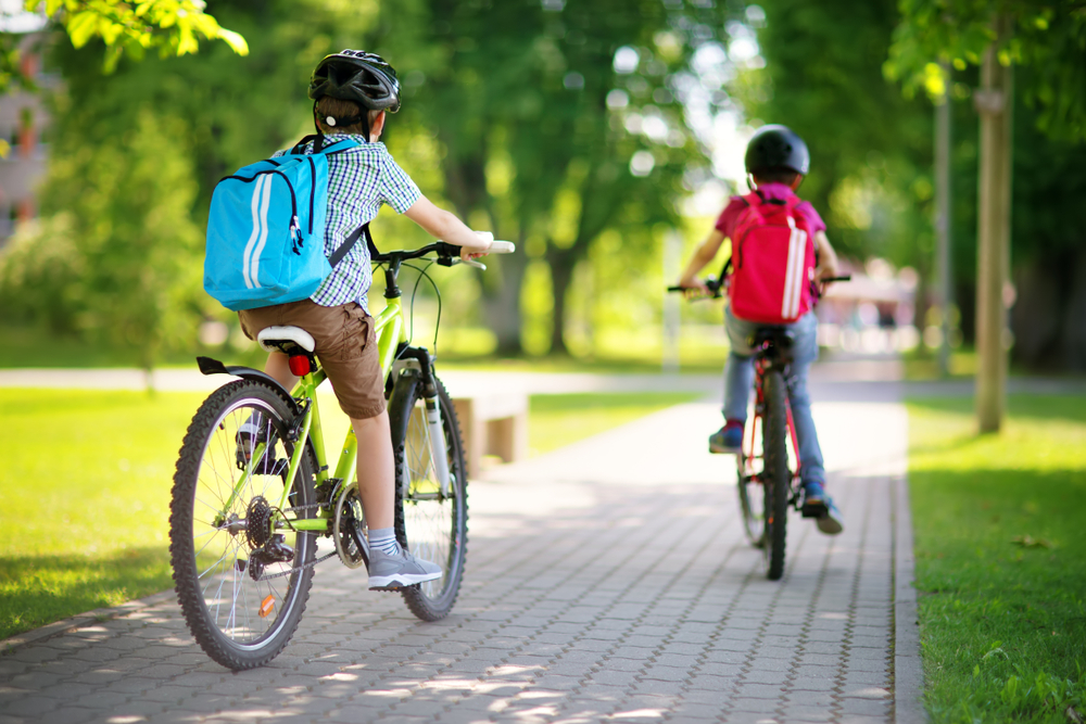 children with rucksacks riding on bikes in the park near school
