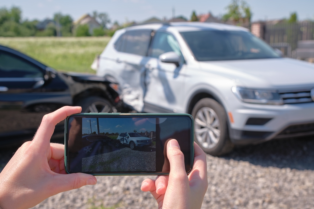 stressed driver taking picture on sellphone camera of smashed vehicle calling for emergency service help after car accident