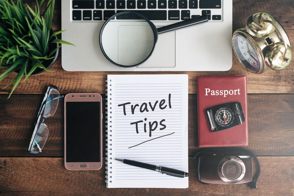 laptop, notebook, smartphone, passport, compass, magnifying glass and clock with travel tips