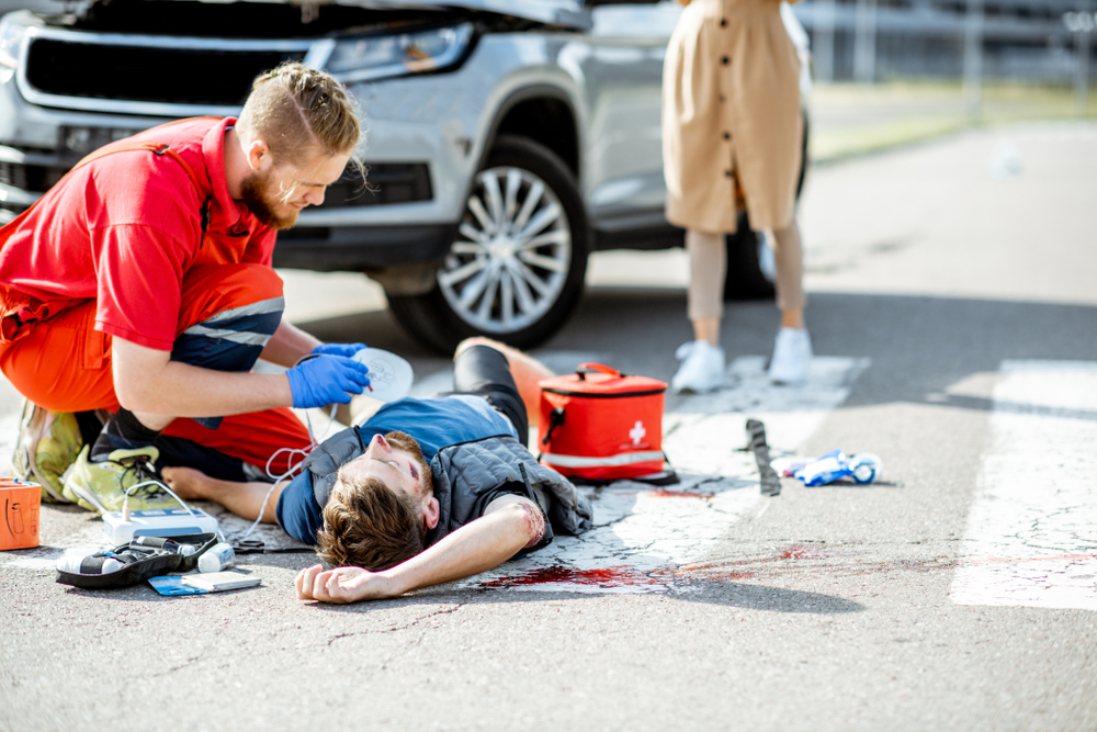 ambluence worker applying emergency care to the injured bleeding man lying on the pedestrian crossing