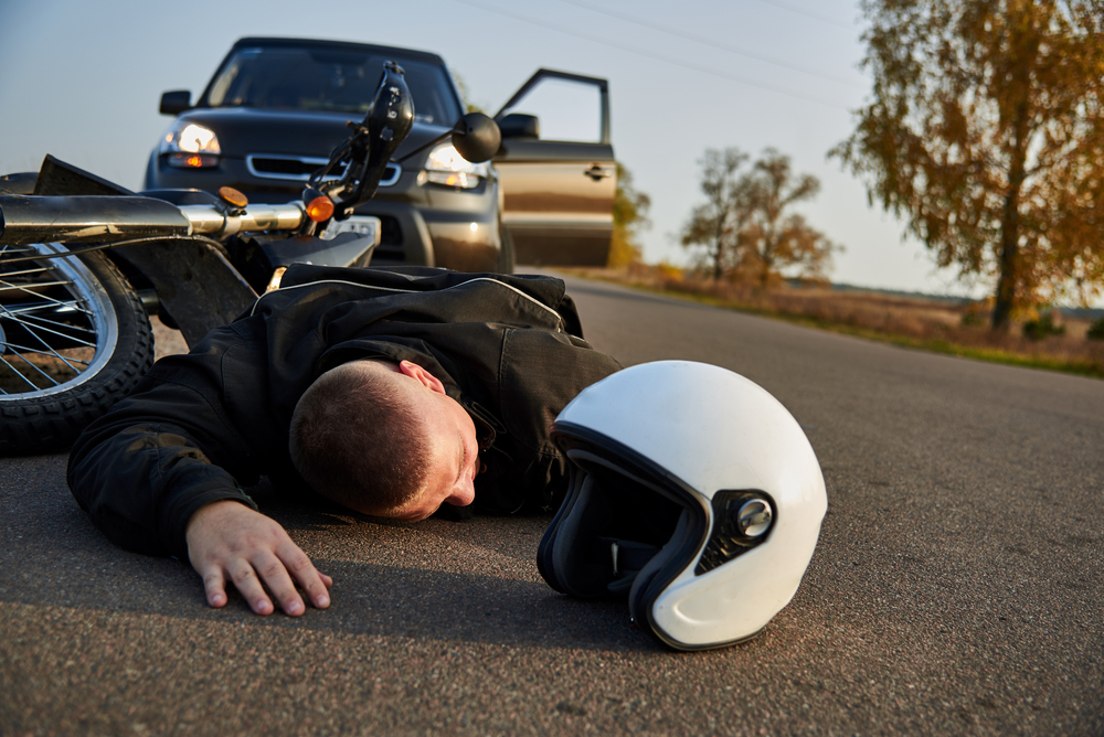 A motorcyclist lies on the asphalt near a motorcycle and car, the theme of road accidents